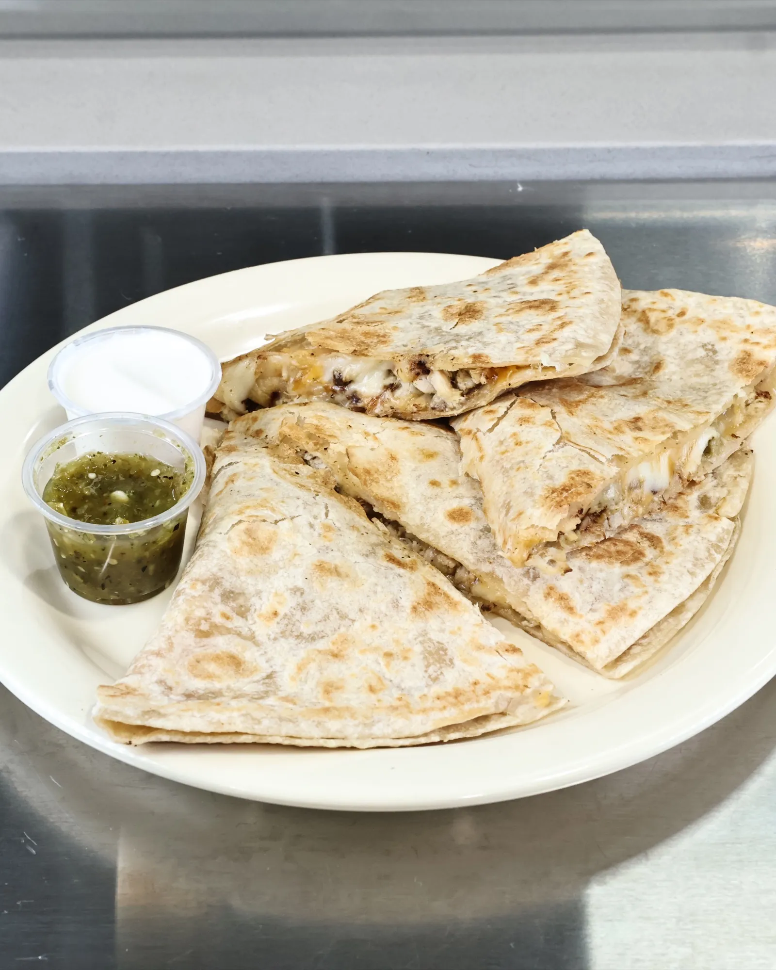 Quesadilla cut into wedges with crema and green salsa