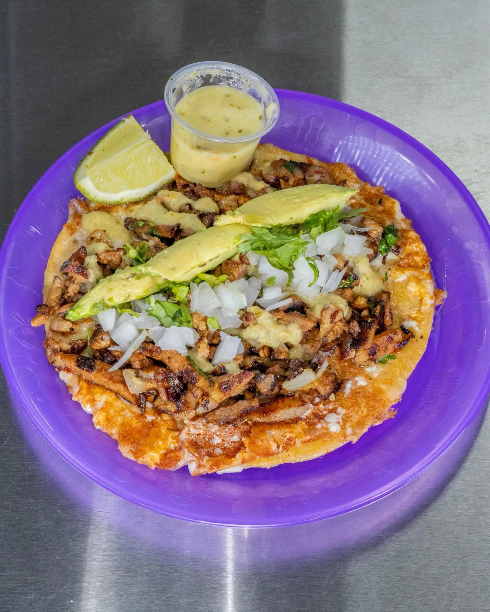 Al pastor taco with avocado, onion and crema on a purple plate, salsa cup and lime