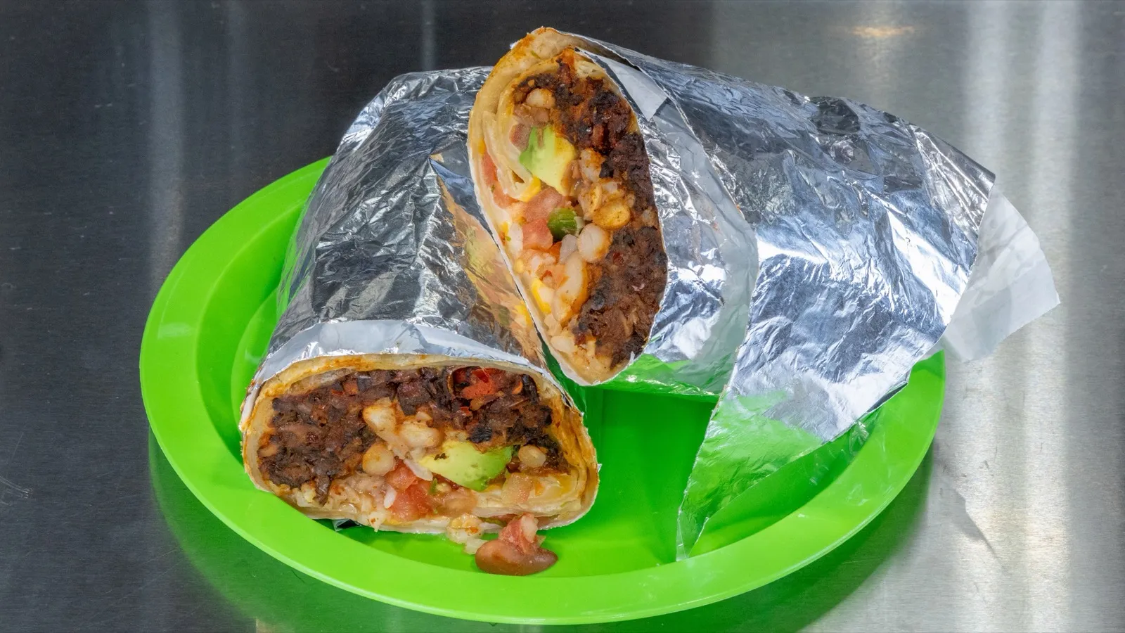 Veggie burrito cut in half, wrapped in foil on a green plate