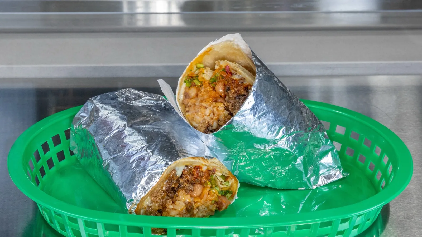 Campechano burrito cut in half, wrapped in foil in a green basket