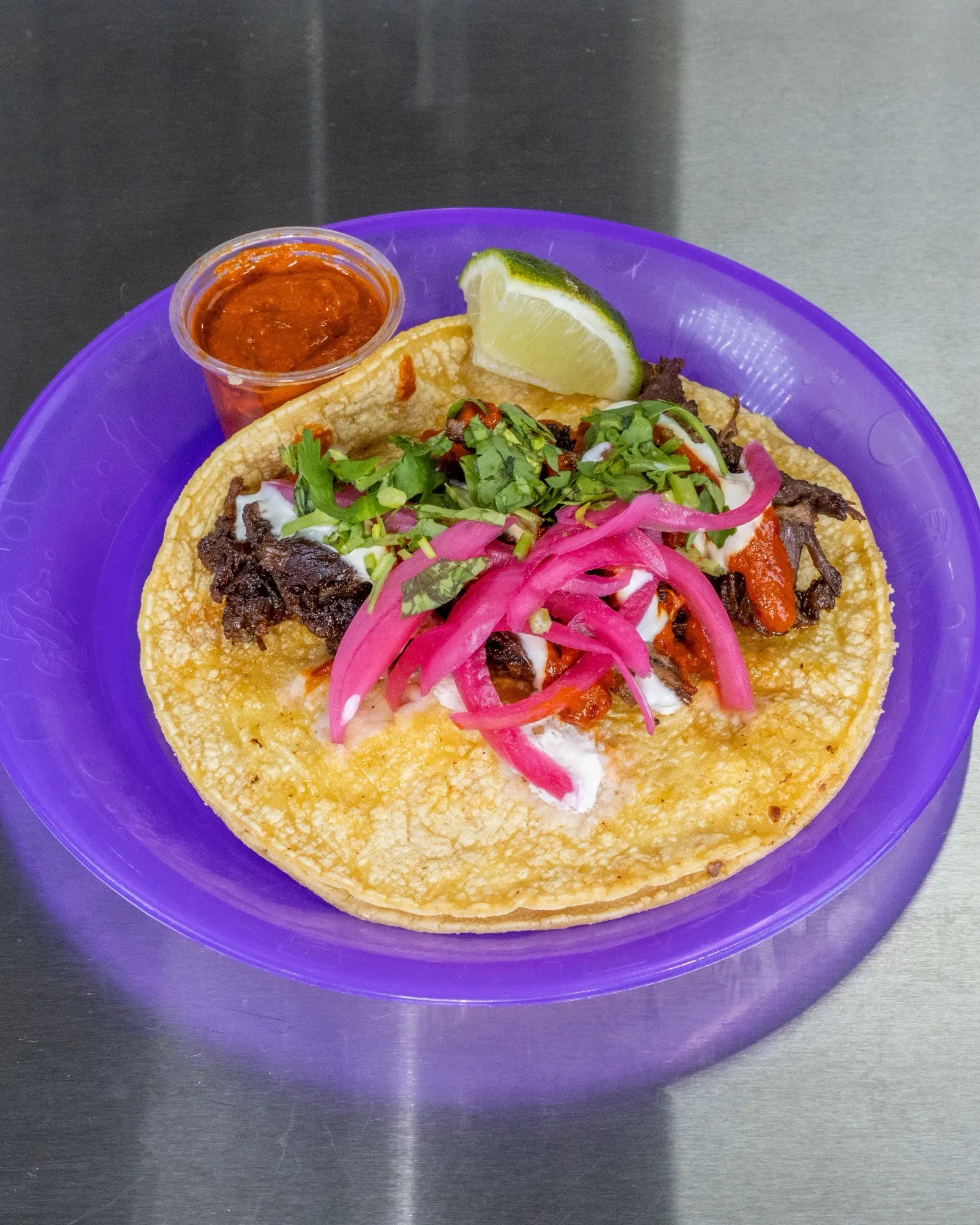 Barbacoa taco topped with pickled red onion and cilantro, red salsa and lime