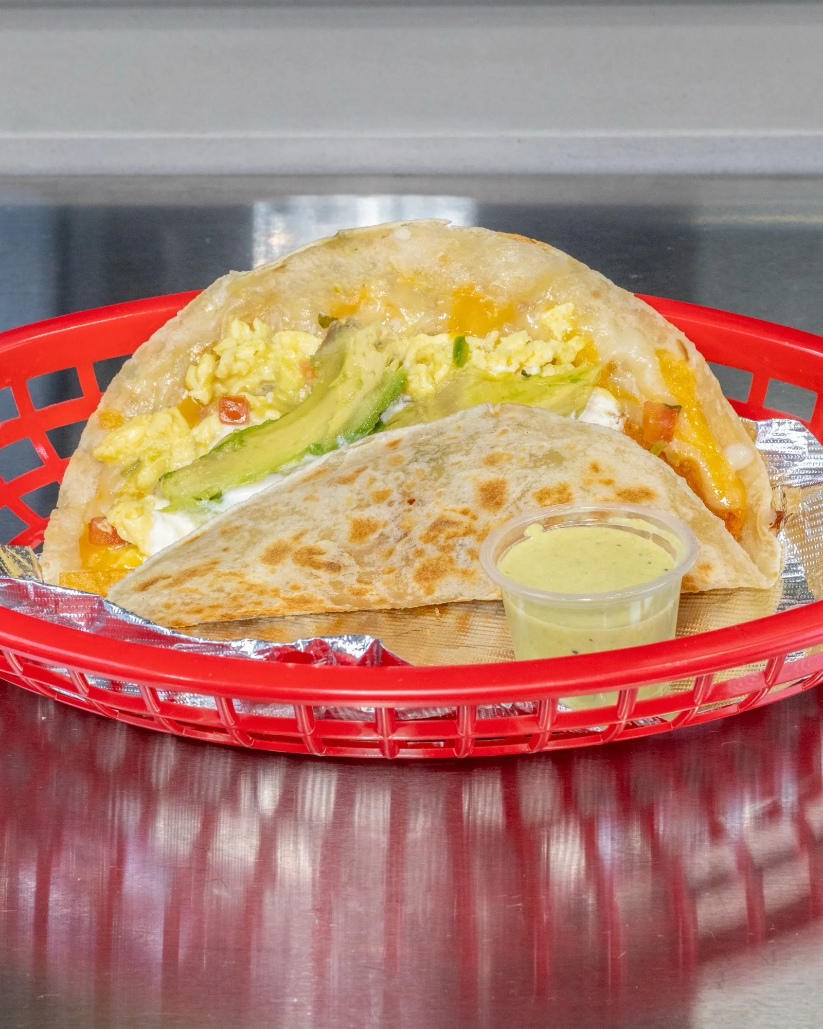 Migas taco with eggs, avocado and crema in a red basket, salsa cup on the side