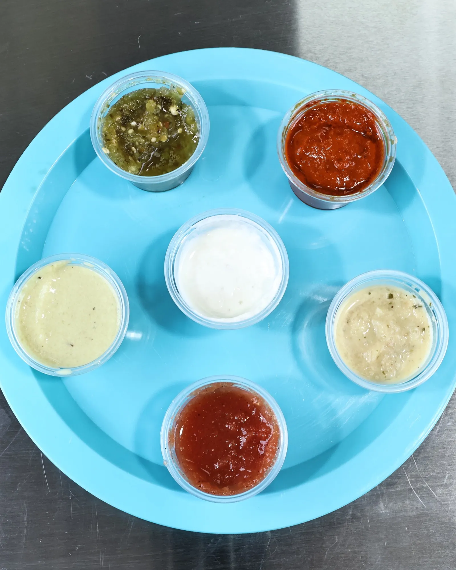 Six house salsas in clear cups on a blue tray